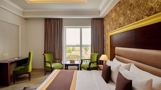 a double bed, armchairs and a coffee table, a work desk, and a chair in the SUPER DELUXE ROOM - Royal Kingdom Sarovar Portico, Pilibhit