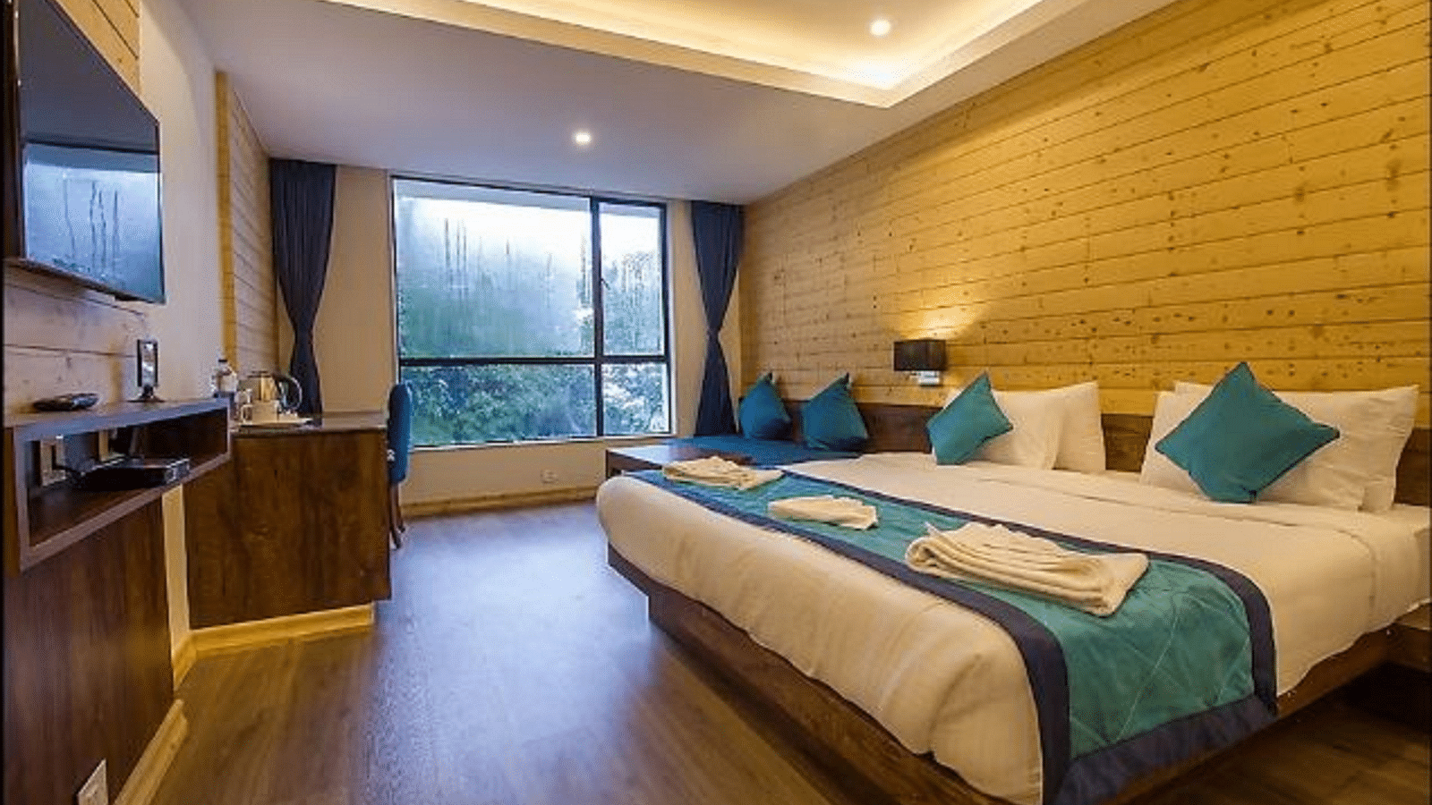 An image of a premium suite with bed, flat screen TV, couch, lamps, an expansive window, and warm lighting - Yashshree Sanderling, Darjeeling