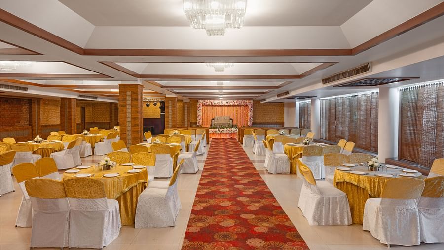 A banquet hall with chairs tied with bows, round tables, a long carpet in the center.- Clarks Inn Express, Near Jammu Bari Brahmana Railway Station.
