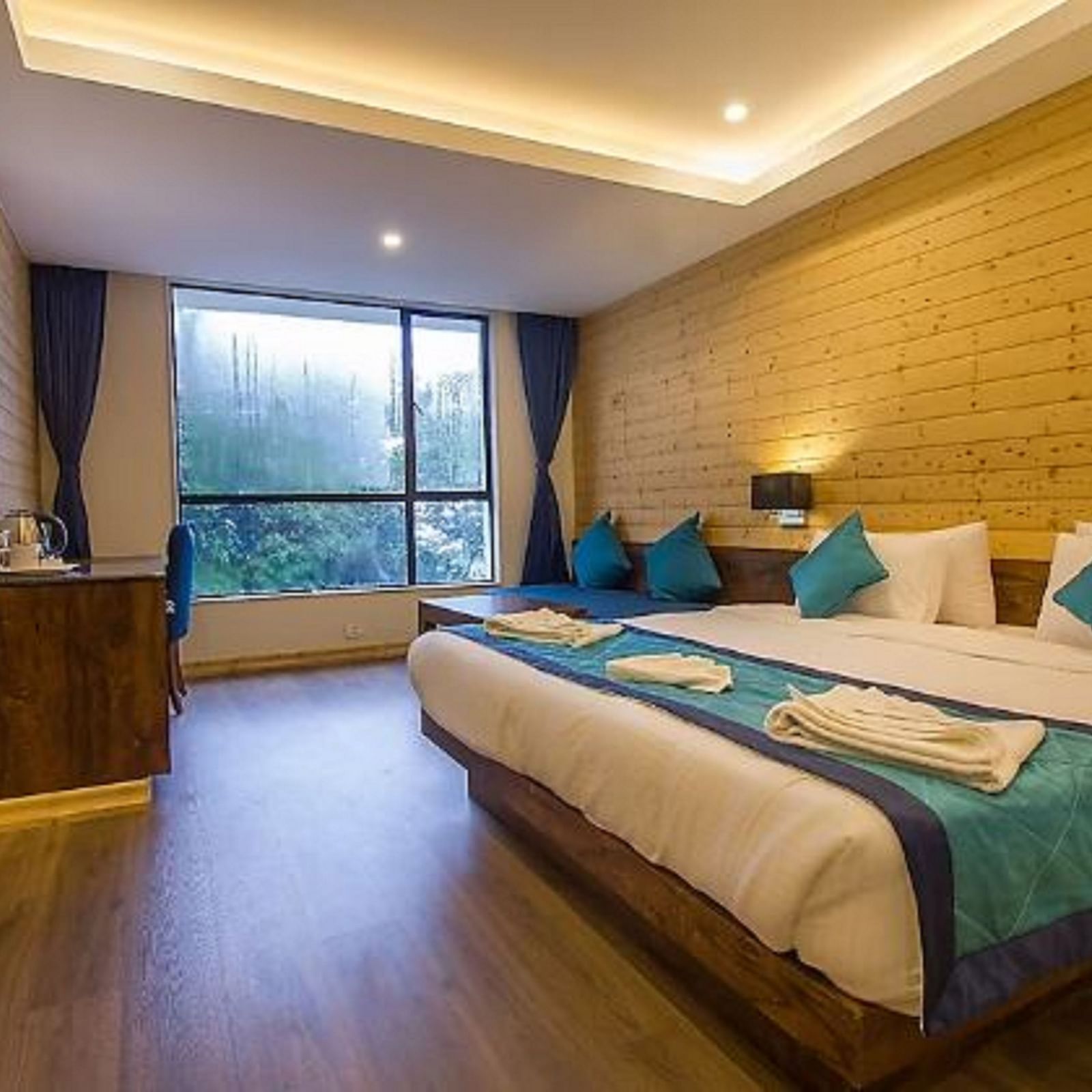 An image of a premium suite with bed, flat screen TV, couch, lamps, an expansive window, and warm lighting - Yashshree Sanderling, Darjeeling
