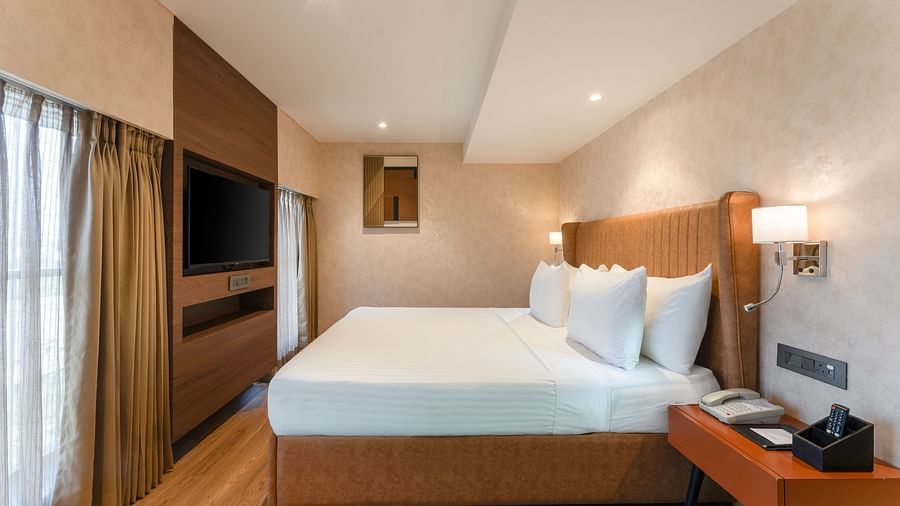Neatly arranged king-size bed in a soft-lit room with bedside tables and large curtained window at Clarks Inn Suites, Hyderabad