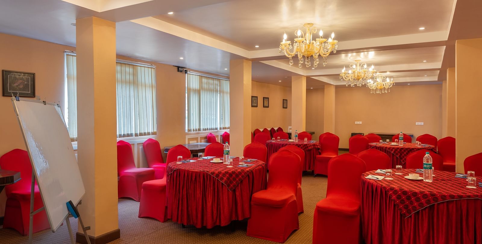 A shot of red tables and chairs in a banquet all at Summit, the room also features chandelers and white board.