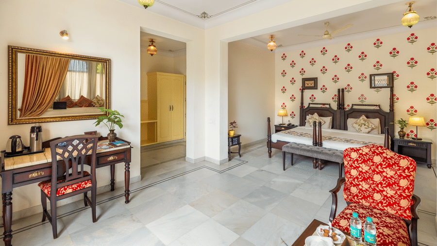 A vanity desk with a mirror stands opposite a bedroom area with twin poster beds at Akshay Niwas Boutique Hotel By Amantra, Udaipur.
