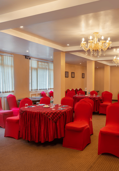 A shot of red tables and chairs in a banquet all at Summit, the room also features chandelers and white board.