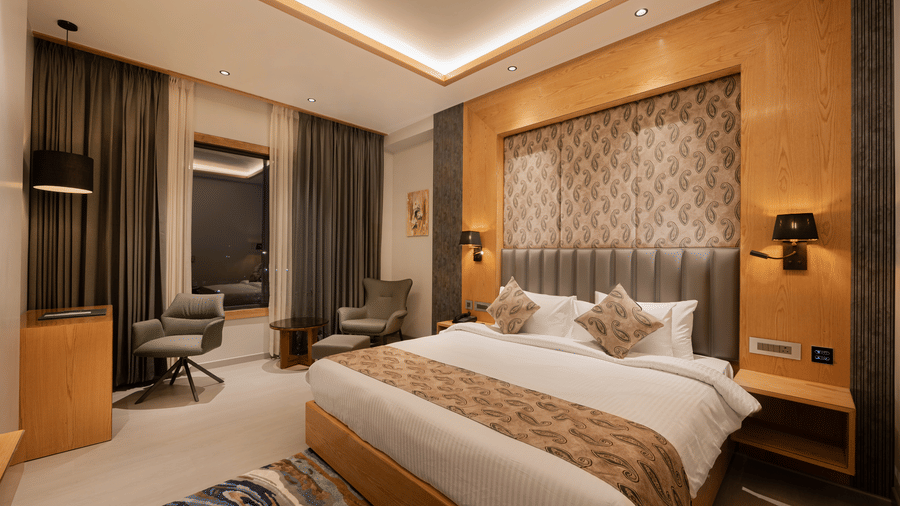 A bright guest room with a king-sized bed, decorative headboard, and warm wooden wall panelling at Ananta Express, Katra.
