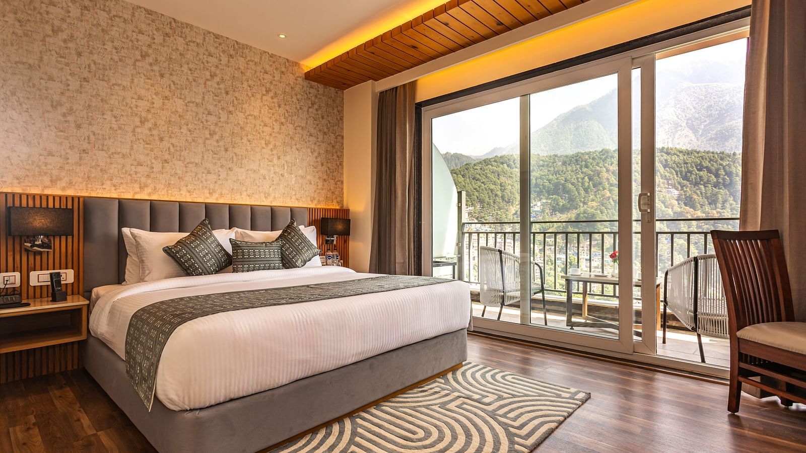 An image of a Suite with a bed, bed side table, lamp shades, and an expansive glass door leading to the balcony - The Belvedere Himalayan Retreat, McLeodganj