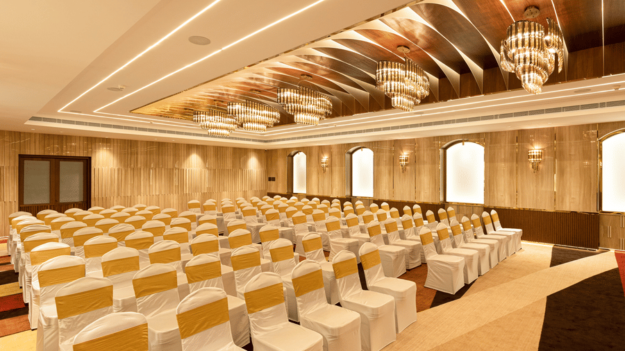 A grand event hall arranged with theatre-style seating featuring white and gold chair covers - Jenneys Residency, Coimbatore