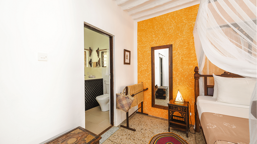 Interior view of a bedroom with an accent wall, a bed with a white canopy, a wooden mirror, and a bathroom visible through an open doorway - Shooting Star Boutique Hotel.