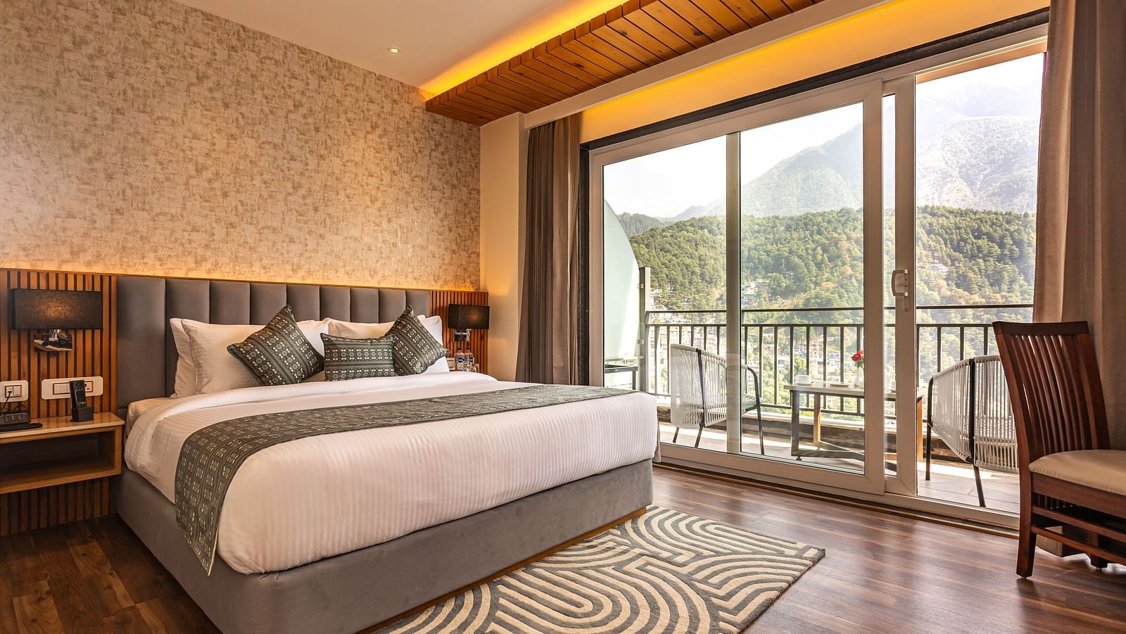 An image of a Suite with a bed, bed side table, lamp shades, and an expansive glass door leading to the balcony - The Belvedere Himalayan Retreat, McLeodganj