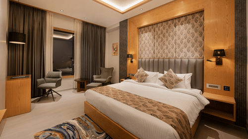 A bright guest room with a king-sized bed, decorative headboard, and warm wooden wall panelling at Ananta Express, Katra.