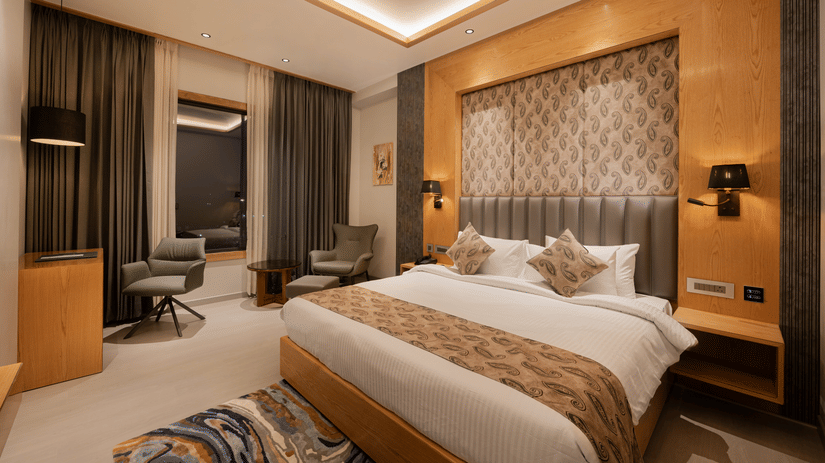 A bright guest room with a king-sized bed, decorative headboard, and warm wooden wall panelling at Ananta Express, Katra.