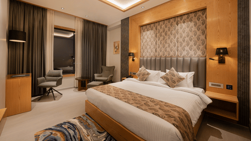 A bright guest room with a king-sized bed, decorative headboard, and warm wooden wall panelling at Ananta Express, Katra.