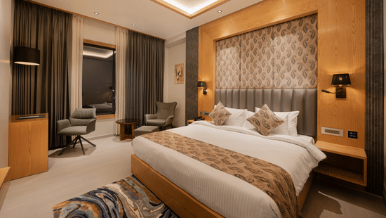 A bright guest room with a king-sized bed, decorative headboard, and warm wooden wall panelling at Ananta Express, Katra.