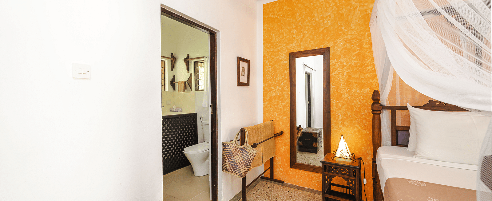 Interior view of a bedroom with an accent wall, a bed with a white canopy, a wooden mirror, and a bathroom visible through an open doorway - Shooting Star Boutique Hotel.