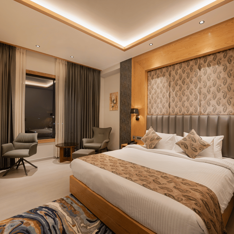 A bright guest room with a king-sized bed, decorative headboard, and warm wooden wall panelling at Ananta Express, Katra.