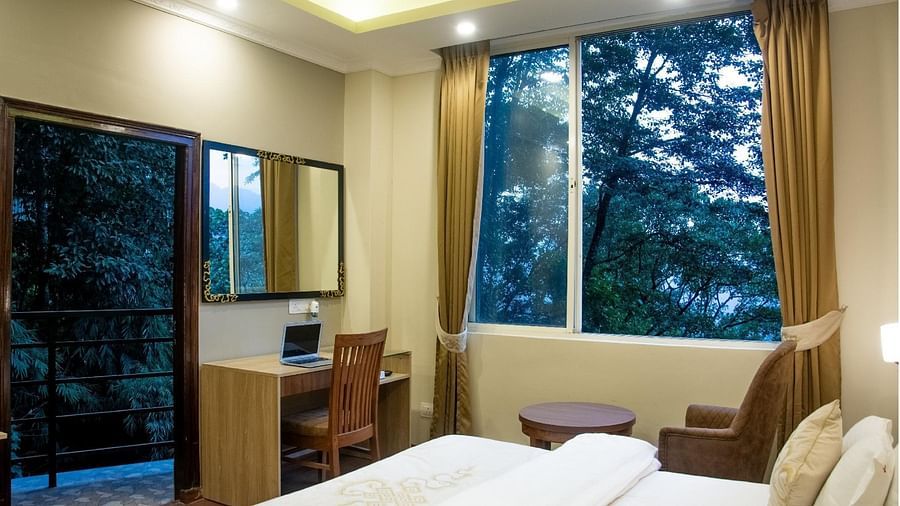 A queen bed, study table, large window and a door leading to the balcony inside Premium Room - Sumitel Gangtok