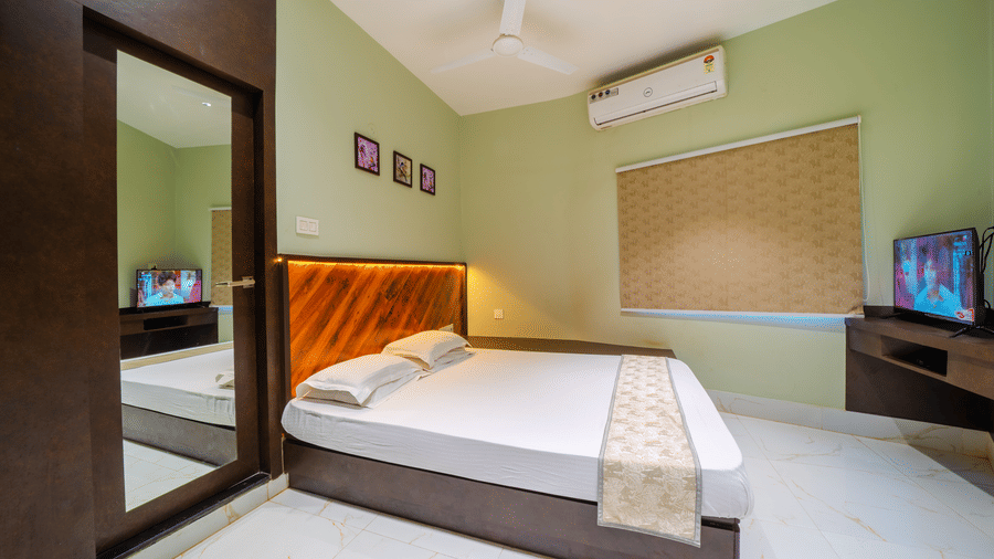 Brightly-lit bedroom with a double bed, light green walls, a mirror, an air conditioner, and a wall-mounted TV - Hotel Dolphin Puri
