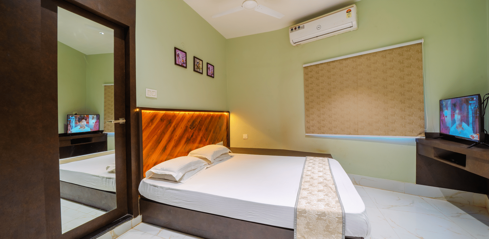 Brightly-lit bedroom with a double bed, light green walls, a mirror, an air conditioner, and a wall-mounted TV - Hotel Dolphin Puri