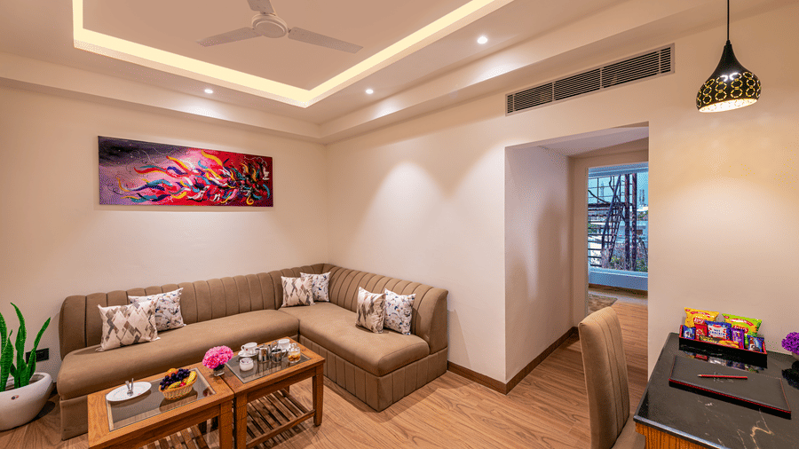 A living space with brown sofas, wooden tables, an abstract art wall, and a chair and a desk under pendant light at Lords Eco Inn Dehradun.