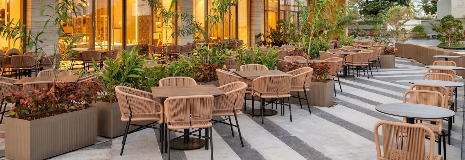Outdoor restaurant seating with warm lighting and landscaped surroundings at Merlis Hotel, Coimbatore.