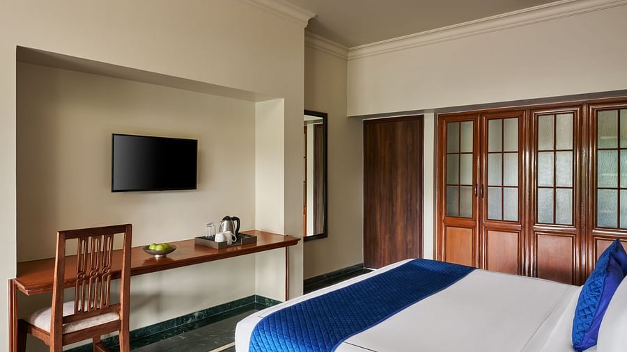 A clean and minimalist Executive Suite with a large bed, wooden furniture, and a wall-mounted television at DGV Resort by Treat, Silvassa