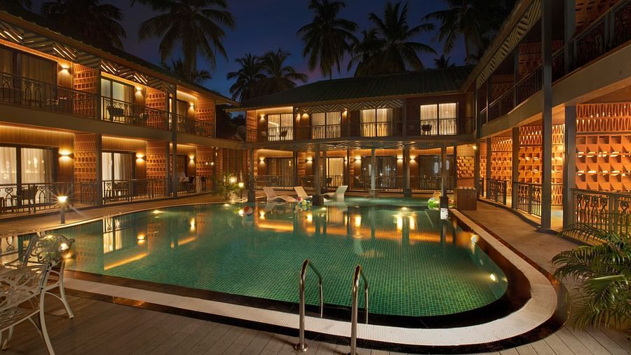 A spacious courtyard with a swimming pool, surrounded by a building with wooden exteriors. The area features several lounge chairs and palm trees, giving the space a relaxing feel - Coral Reef Resort & Spa, Havelock