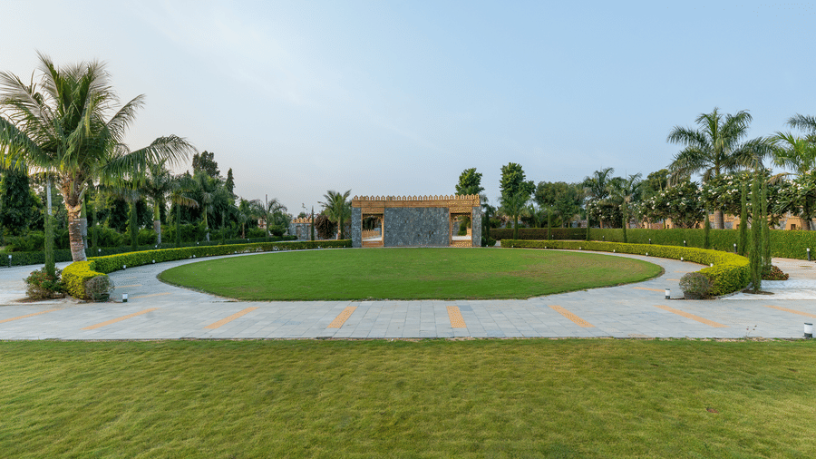 An expansive circular green lawn at EsthereaRaj Leela, Ranakpur, surrounded by a paved walking path and palm trees.