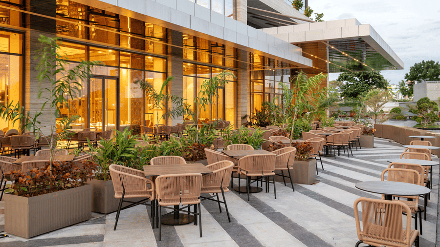 Outdoor seating with warm lighting, tiled flooring, and landscaped surroundings at Mercafe inside Merlis Hotel, Coimbatore.