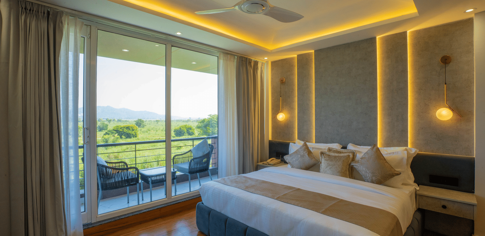 A guest room at Sukoon by the Ganges featuring a large bed, ambient lighting, and floor-to-ceiling balcony doors.