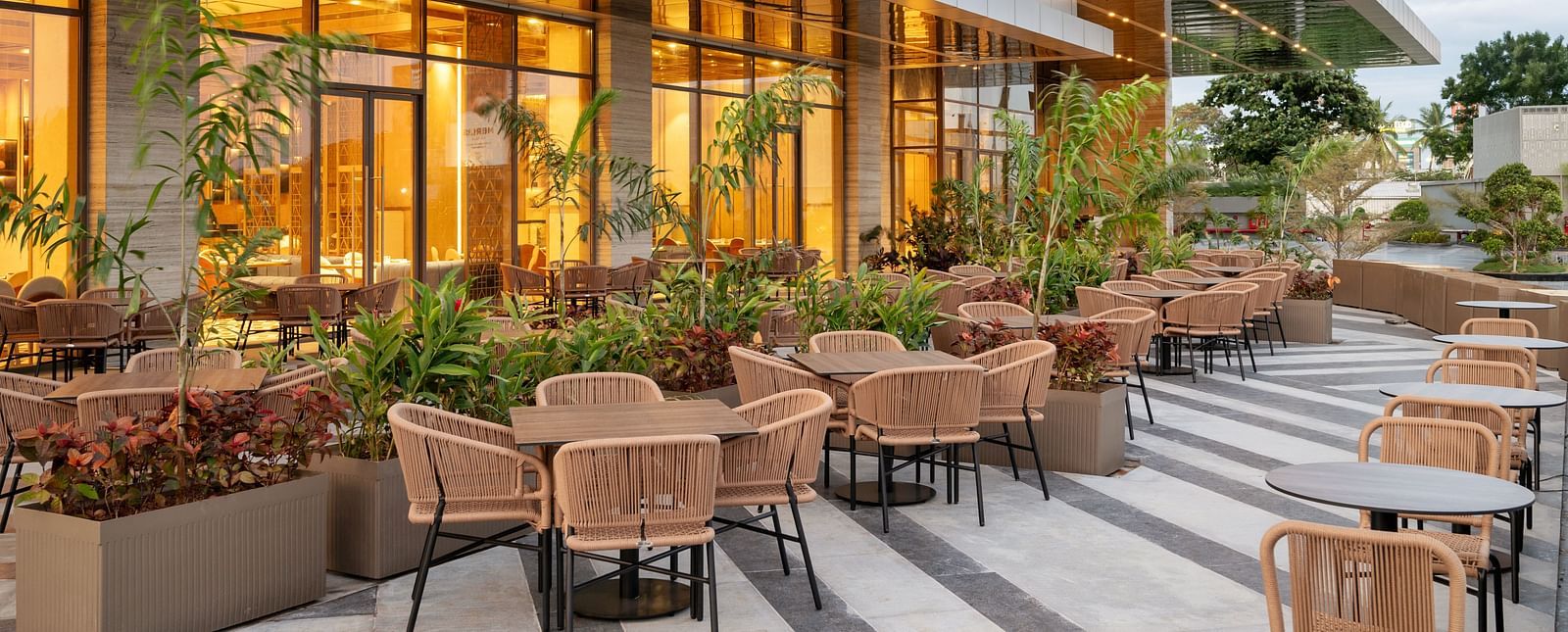 Outdoor restaurant seating with warm lighting and landscaped surroundings at Merlis Hotel, Coimbatore.