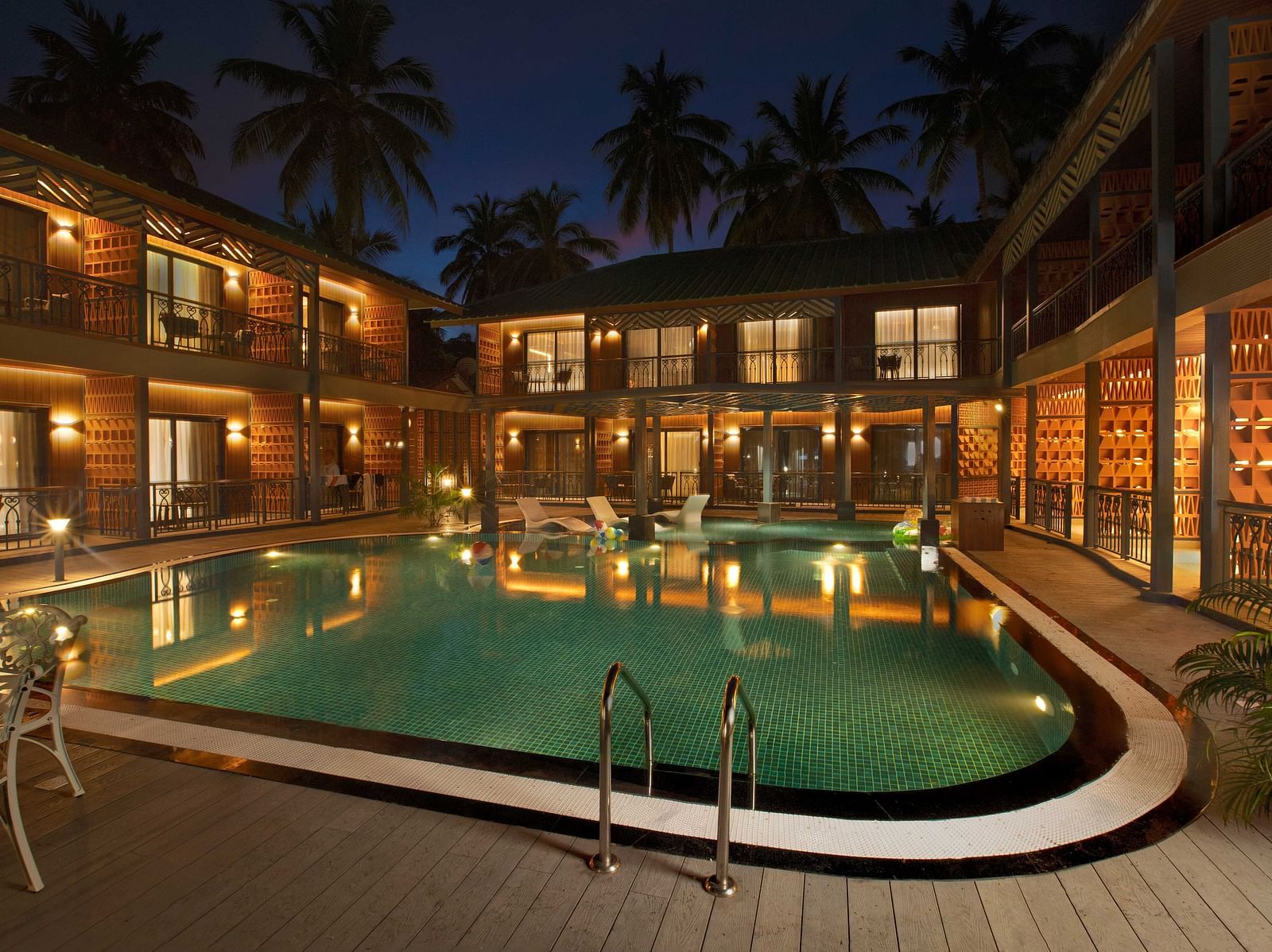 A spacious courtyard with a swimming pool, surrounded by a building with wooden exteriors. The area features several lounge chairs and palm trees, giving the space a relaxing feel - Coral Reef Resort & Spa, Havelock