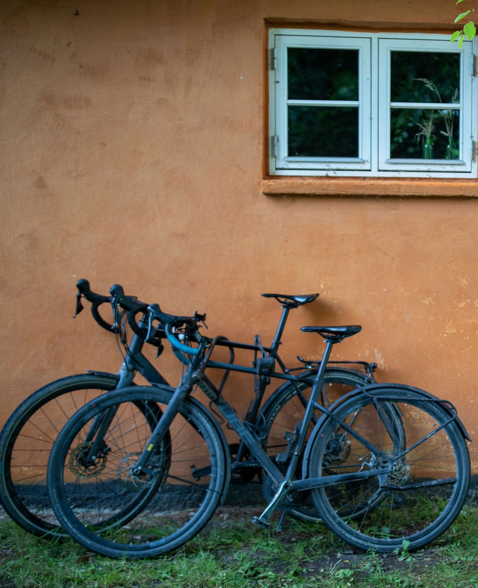 Two bicycles parked against an orange wall below a window.