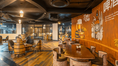 Rhythm & Brews with a rustic ambience, featuring wooden barrels, high tables with stools, and walls adorned with brewery-related artwork at The Qualia Resort Club & Brewery, Udaipur.