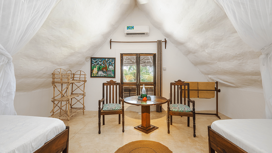 View of two beds and a table with two chairs with a door and air-conditioner in the background in Sea View Family Cottages - Shooting Star Boutique Hotel.
