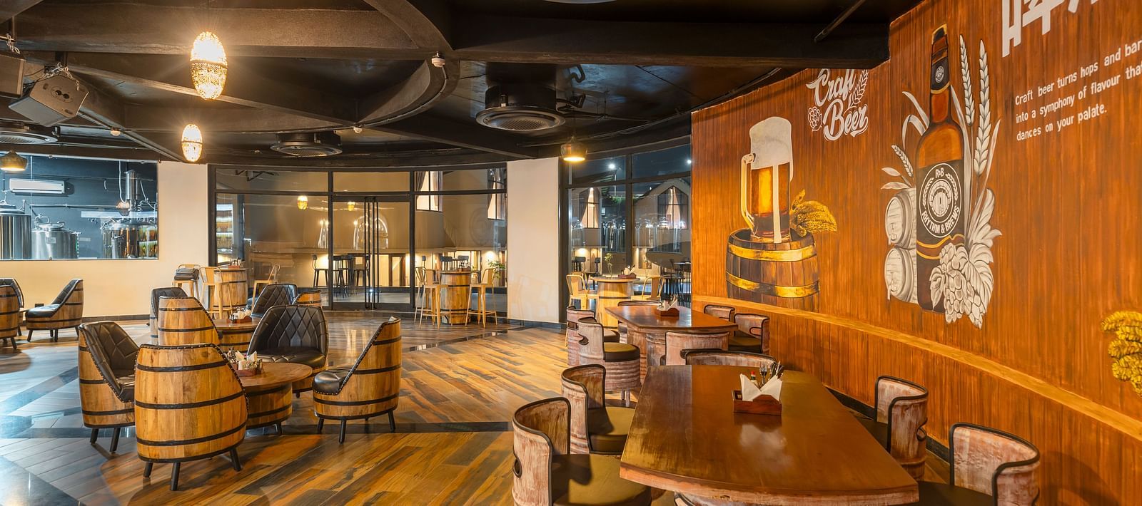 Rhythm & Brews with a rustic ambience, featuring wooden barrels, high tables with stools, and walls adorned with brewery-related artwork at The Qualia Resort Club & Brewery, Udaipur.