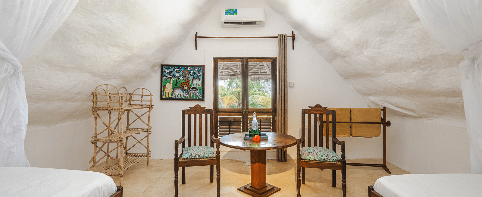 View of two beds and a table with two chairs with a door and air-conditioner in the background in Sea View Family Cottages - Shooting Star Boutique Hotel.