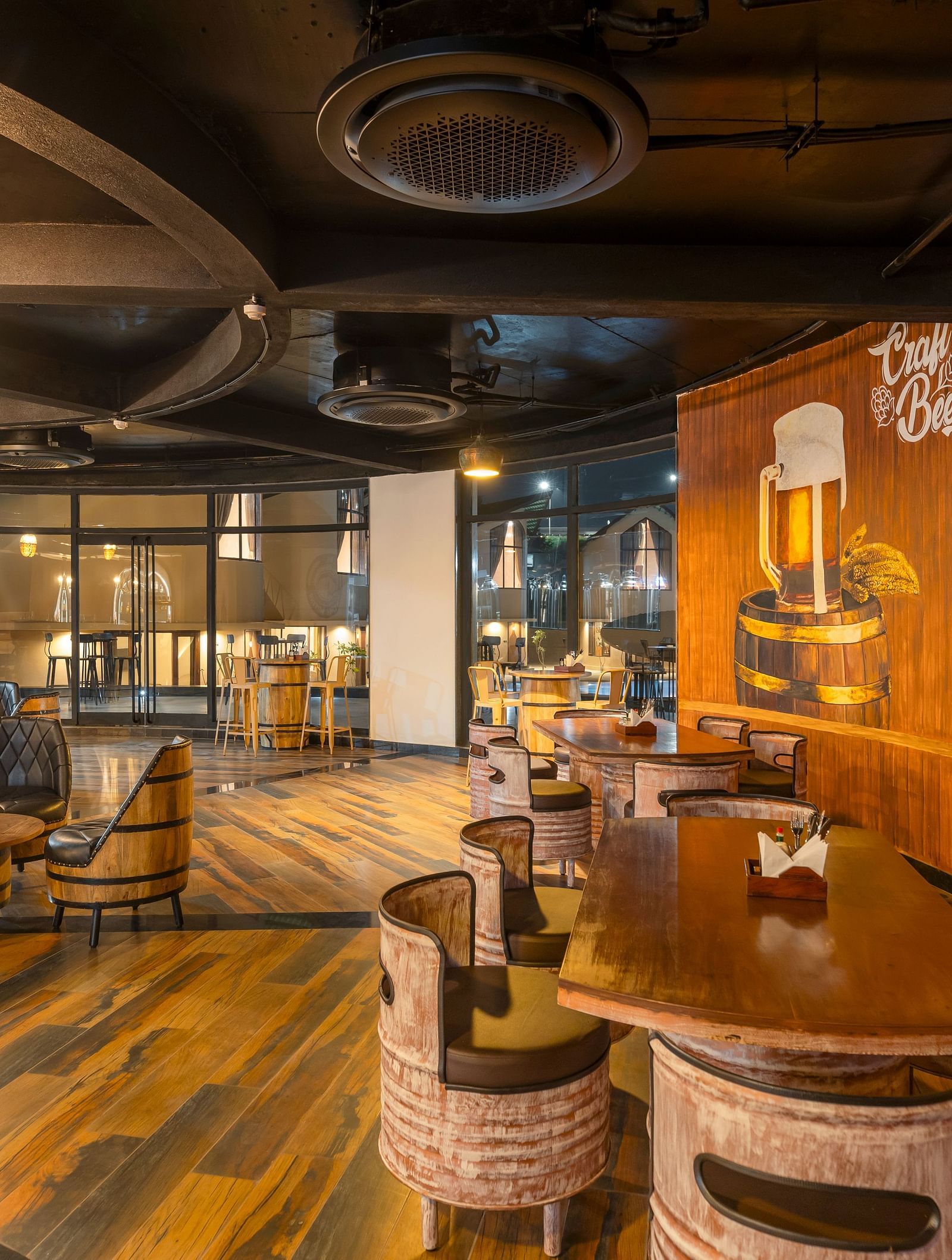Rhythm & Brews with a rustic ambience, featuring wooden barrels, high tables with stools, and walls adorned with brewery-related artwork at The Qualia Resort Club & Brewery, Udaipur.