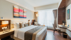 A modern bedroom at Nirvana Sarovar Portico, Gorakhpur featuring a king-size bed, abstract wall art, study desk, and large window.