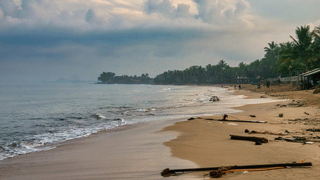 A quiet beach with sand and rocks leading to the sea under a cloudy sky.