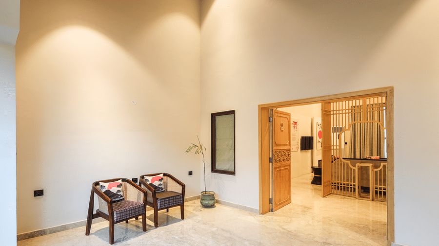 An interior shows chairs with a table placed near a wall, a doorway and lighting fixtures above at Ananta Spa & Resort, Jaipur.