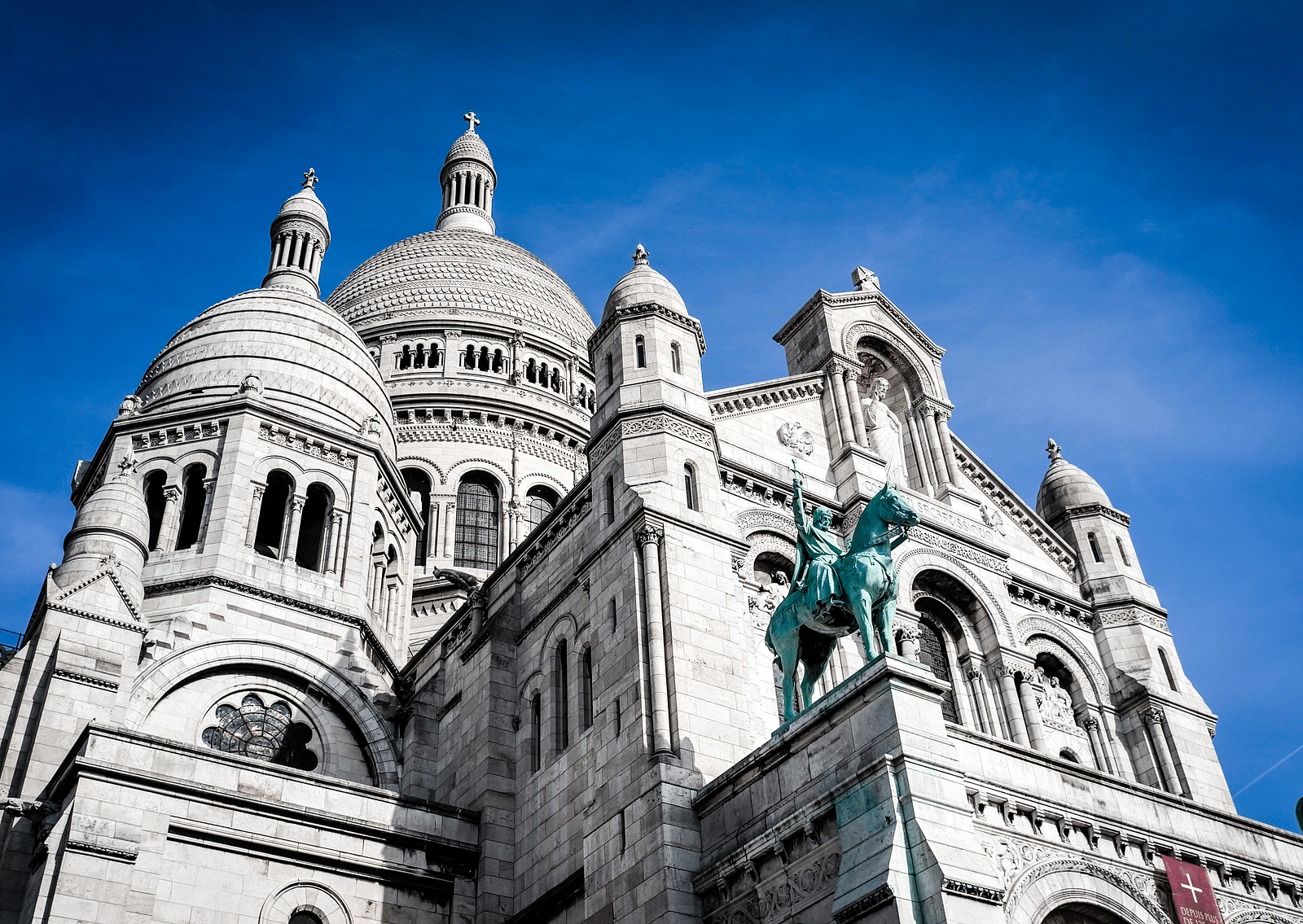 A view from below of a cathedral with many domes and a blue sky in the background.