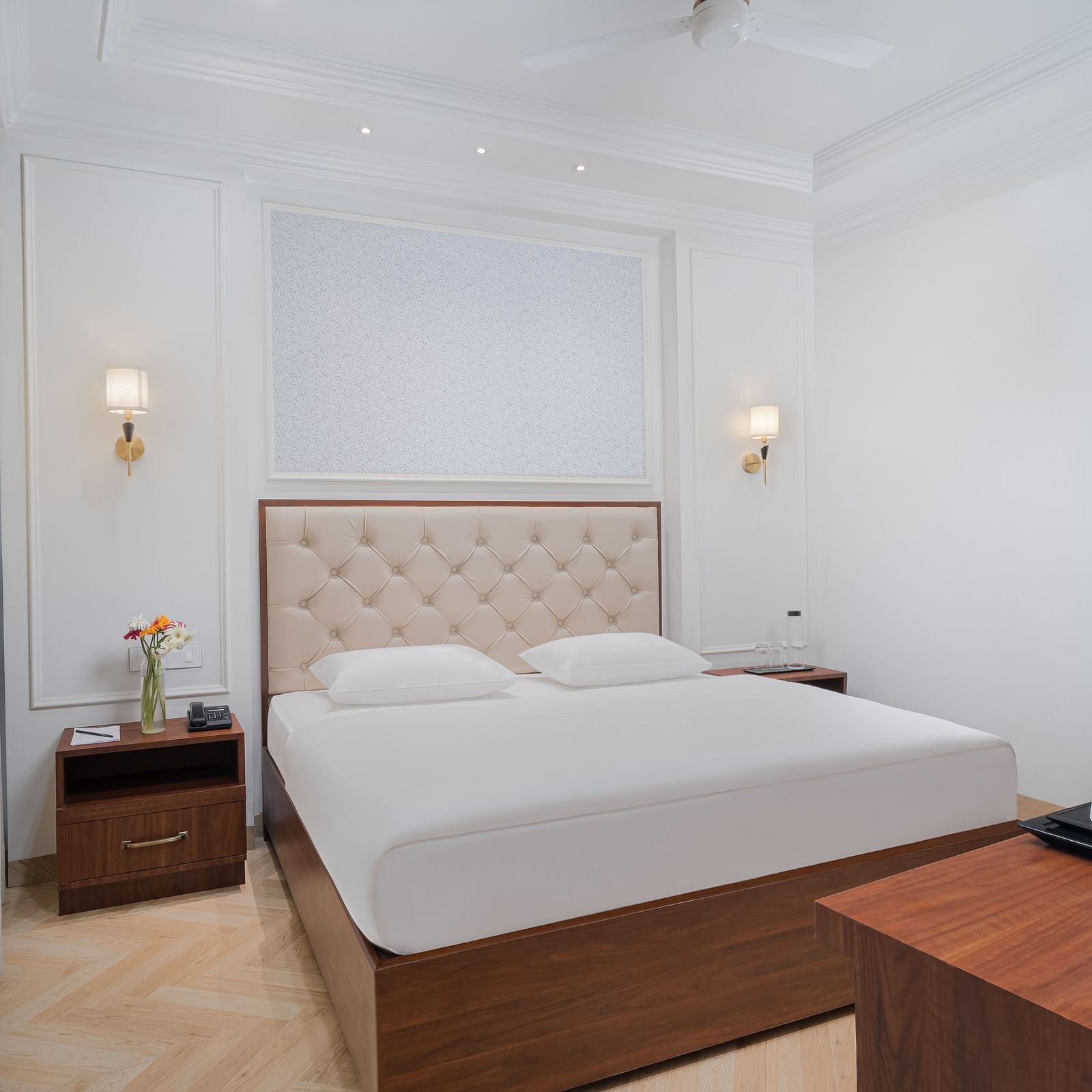 A spacious bed featuring a cushioned headboard, with bedside tables on either side, and a wooden table holding a tray with a kettle and cups | Hotel Ganga Maiya