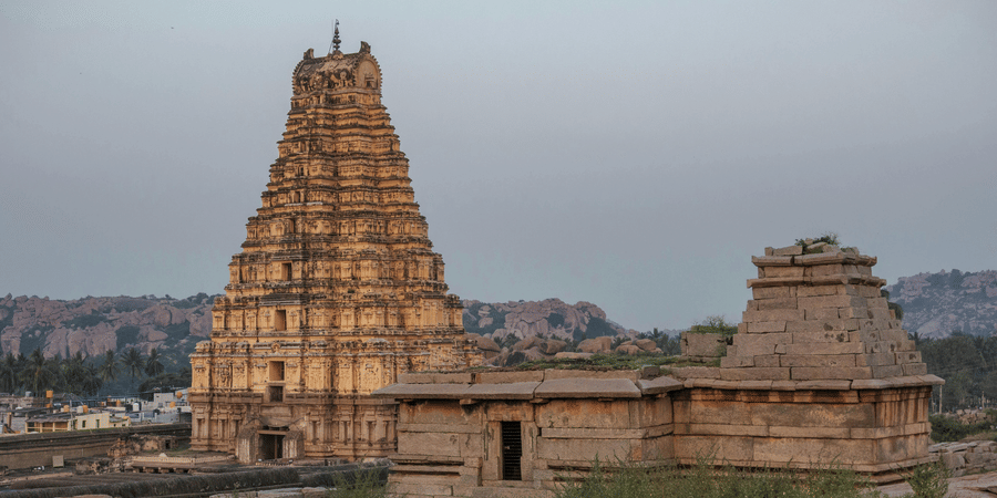 Wide shot of a large, ancient Indian temple gopuram's in Hampi against a cloudy sky.