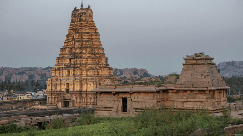 Wide shot of a large, ancient Indian temple gopuram's in Hampi against a cloudy sky.