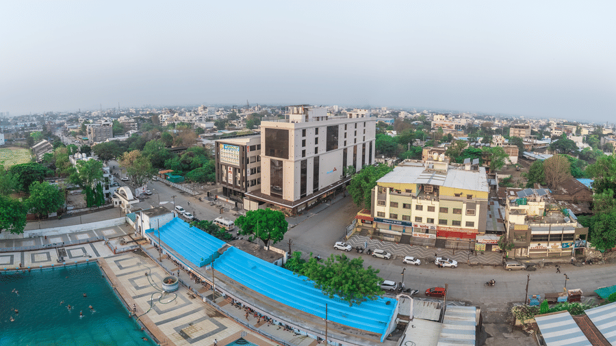  A high-angle view showing a large swimming pool with bright blue seating, neighbouring buildings, and city streets under a hazy sky - Skkylight Lords Inn, Nanded