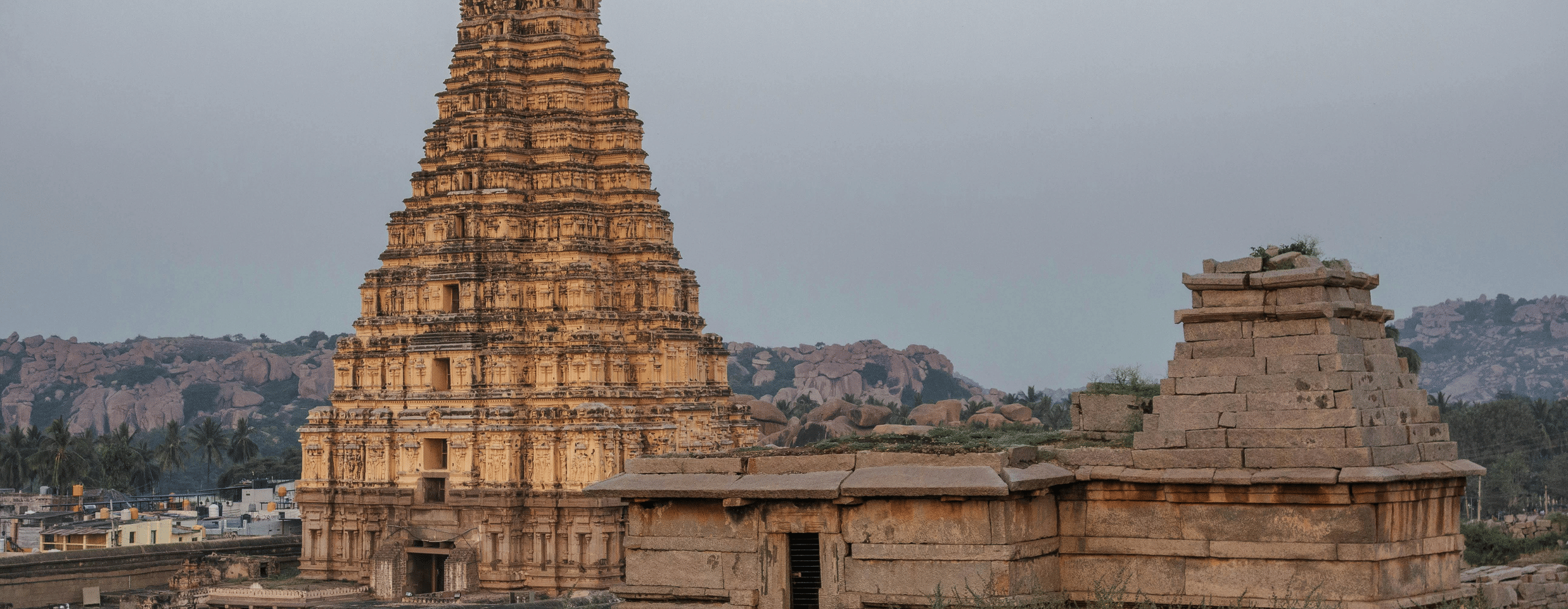 Wide shot of a large, ancient Indian temple gopuram's in Hampi against a cloudy sky.