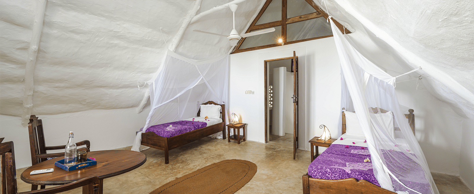 A spacious tented room with decorative bedding, and wooden furniture, featuring two single beds in Sea View Family Cottages - Shooting Star Boutique Hotel