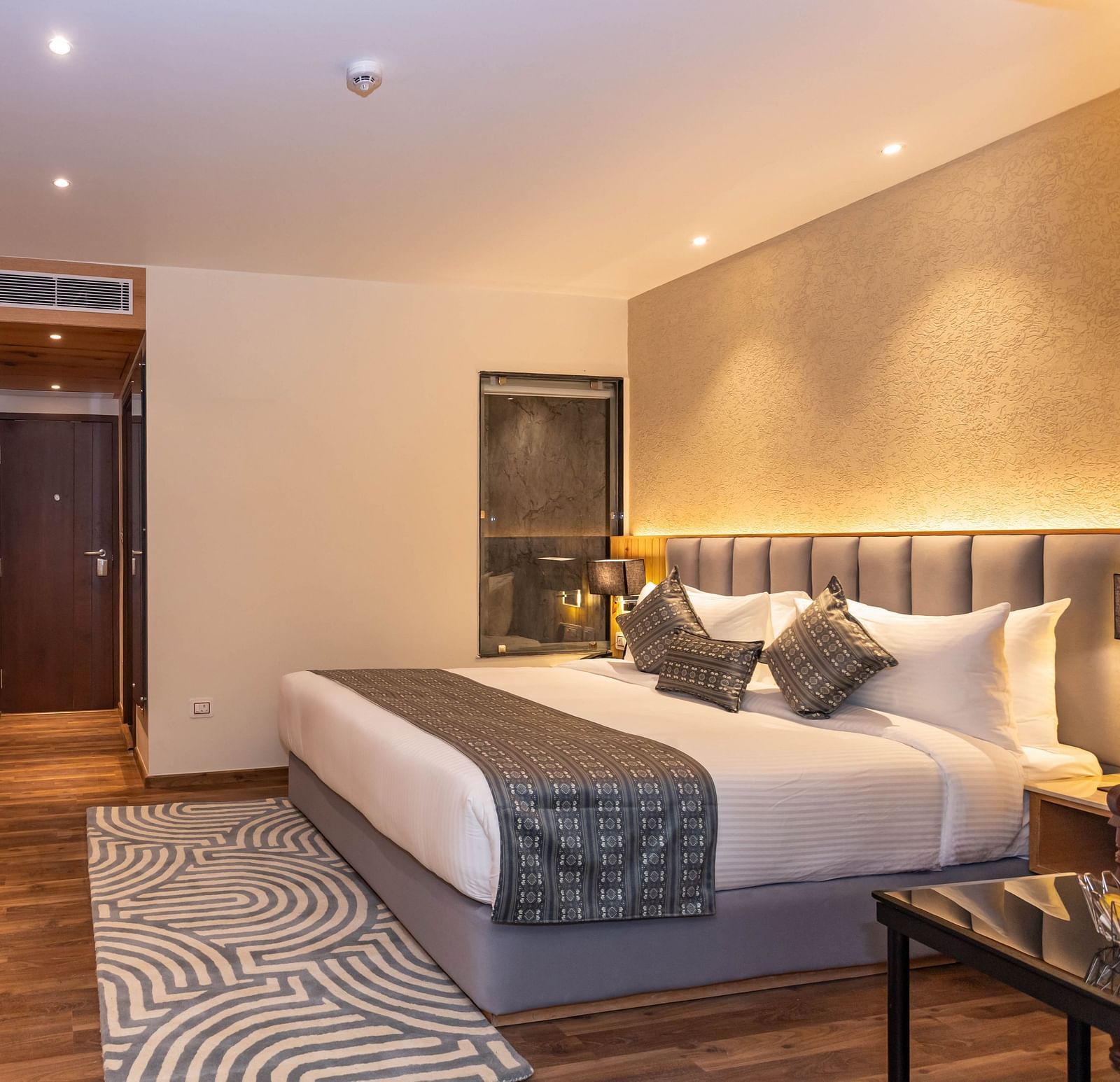 An image of a Deluxe Room with a king size bed, bed side table, work desk and chair, sofa and table, and beautifully decorated room with lighting -  The Belvedere Himalayan Retreat, McLeodganj