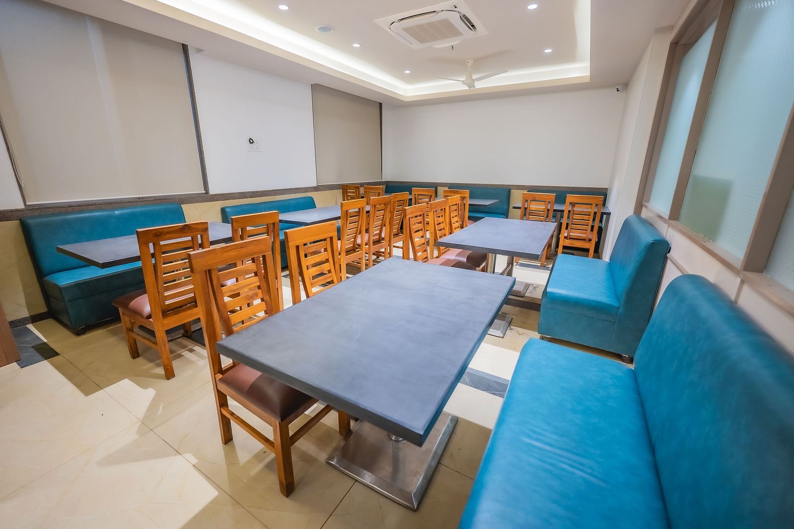 A bright dining room with blue upholstered sofas and several square wooden dining tables with chairs | Lotus Leaf Boutique Hotel