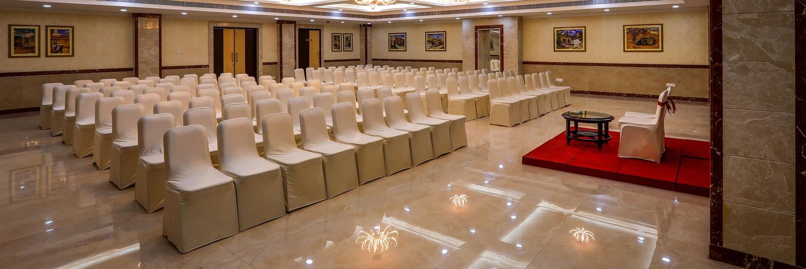 Front view of white chairs and a well-lit ceiling at Banquet Hall in Hotel Aadithya, Chennai